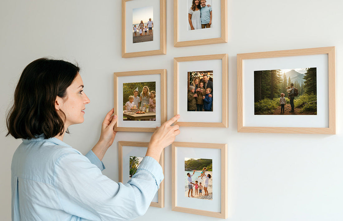 A woman hangs a photo tile on a living room wall using a damage-free method, surrounded by minimalistic wall art and cozy home decor.