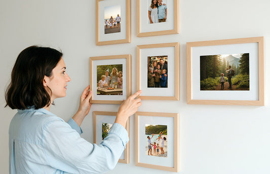 A woman hangs a photo tile on a living room wall using a damage-free method, surrounded by minimalistic wall art and cozy home decor.
